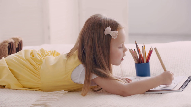 Side view of child drawing with colorful pencils on bed - Footage, Video