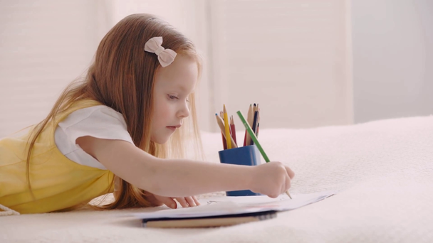 Side view of cute child drawing with pencils and paper on bed - Footage, Video