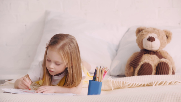 Kid drawing on bed by teddy bear on pillow - Footage, Video