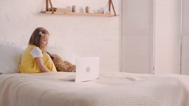 Kind sieht Cartoons am Laptop neben Teddybär im Bett - Filmmaterial, Video