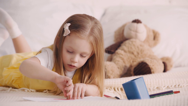 Kid drawing with pencils beside teddy bear on pillow - Footage, Video