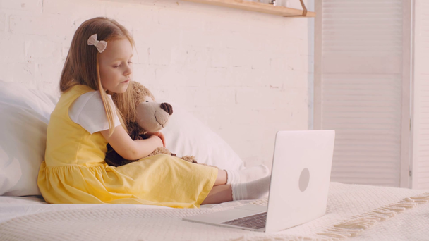 Kid met teddybeer kijken cartoons op laptop en gapen op bed - Video
