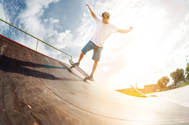 Portrait of a young skateboarder doing a trick on his skateboard on a halfpipe ramp in a skate park in the summer on a sunny day. The concept of youth culture of leisure and sports - Valokuva, kuva