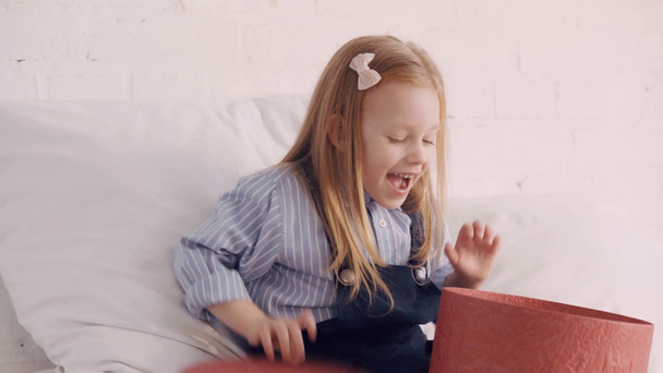 Wesoły dzieciak z pudełkiem prezentów na łóżku - Materiał filmowy, wideo