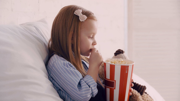 Child with popcorn and teddy bear on bed - Footage, Video