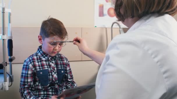 Szemészi kezelés - egy kisfiú szemének ellenőrzése - egy fiú, aki különböző lencséken keresztül olvassa a táblagépből származó betűket - Felvétel, videó
