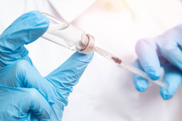 Médico mão segurando seringa e vacina em luvas azuis casaco branco, luz solar. Injeção de doença conceito
 - Foto, Imagem