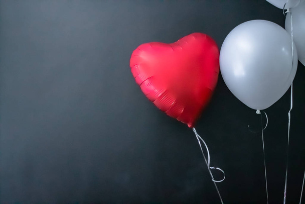 Red heart-shaped balloon and white round air balloon on a black background. valentines day, love. - Φωτογραφία, εικόνα