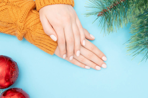 Mãos bonitas femininas com manicura em pregos em suéter quente com bola de Natal vermelha ano novo em fundo azul. Vista superior
 - Foto, Imagem