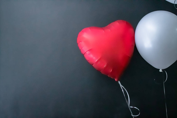 Red heart-shaped balloon and white round air balloon on a black background. valentines day, love. - Φωτογραφία, εικόνα