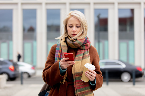 Piękna blondynka z filiżanką kawy za pomocą telefonu komórkowego - Zdjęcie, obraz
