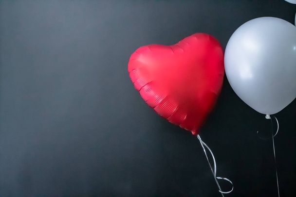 Червона повітряна куля у формі серця та біла кругла повітряна куля на чорному тлі. День валентинки, любов
. - Фото, зображення