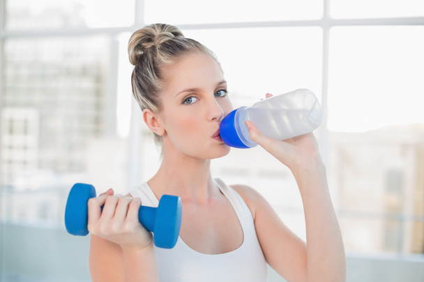 Sporty blonde drinking water while lifting dumbbell - Fotografie, Obrázek