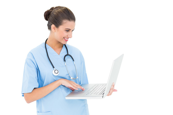 Happy nurse in blue scrubs using a laptop - Фото, изображение
