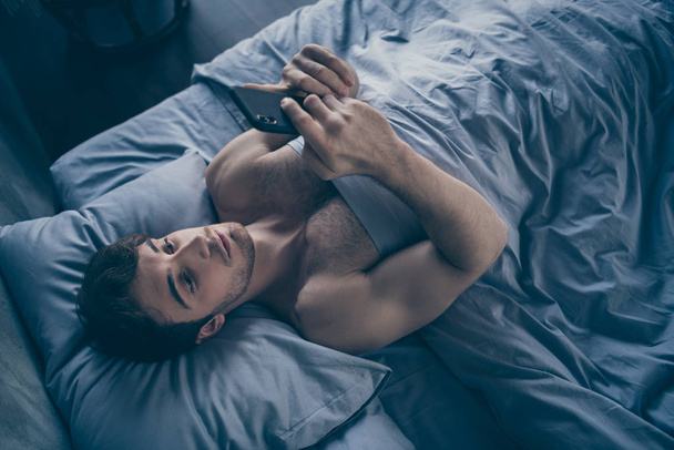 High angle above view photo of handsome homey macho guy lying morning bed alone holding telephone sending message lover mistress calling home visit him sheets room indoors - Фото, зображення