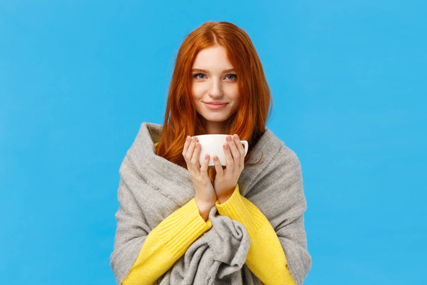 Gyönyörű, romantikus csinos vörös hajú nő szürke sállal, egyre melegebb, ivás forró tea, kezében csésze kávét, mosolygós fényképezőgép örömteli és nyugodt, álló kék háttér elégedett - Fotó, kép