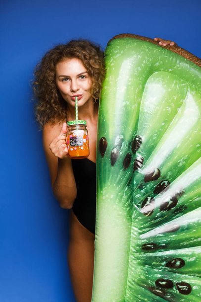 pretty young woman dressed in swimsuit and posing with float kiwi  - Foto, Imagen