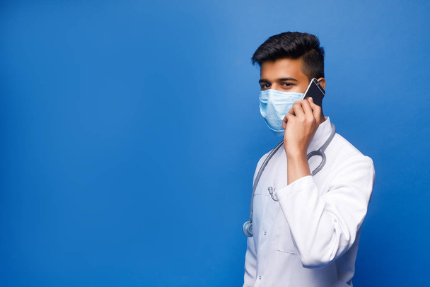 indian male doctor in white coat on blue background - Φωτογραφία, εικόνα
