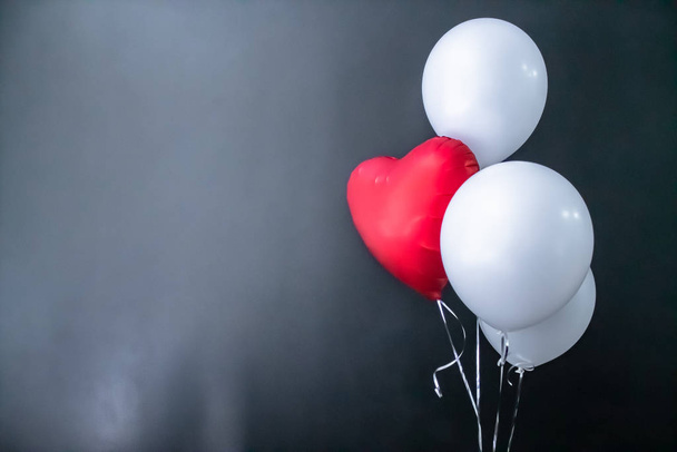 Κόκκινο μπαλόνι σε σχήμα καρδιάς και λευκά στρογγυλά αερόστατα σε μαύρο φόντο. Ημέρα του Αγίου Βαλεντίνου, διακοπές, αγάπη. - Φωτογραφία, εικόνα