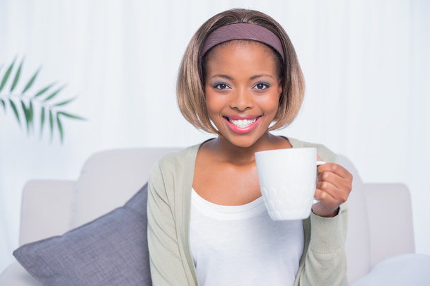Smiling woman sitting on sofa holding mug of coffee - Valokuva, kuva