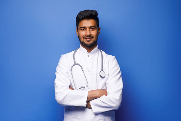 indian male doctor in white coat on blue background - Foto, afbeelding