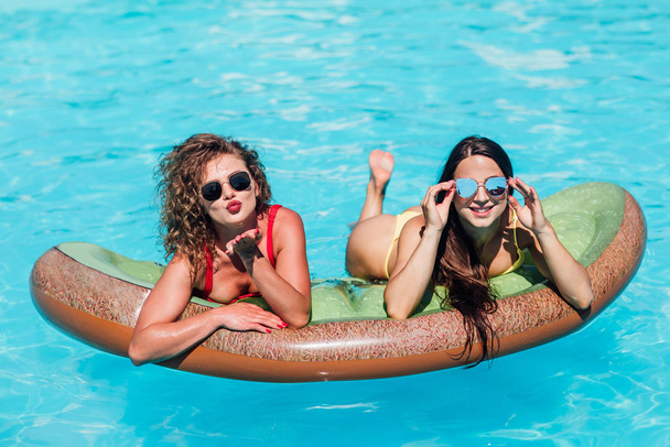 Portrait of pretty female friends wearing bikini lying on inflatable toy kiwi  - Foto, imagen
