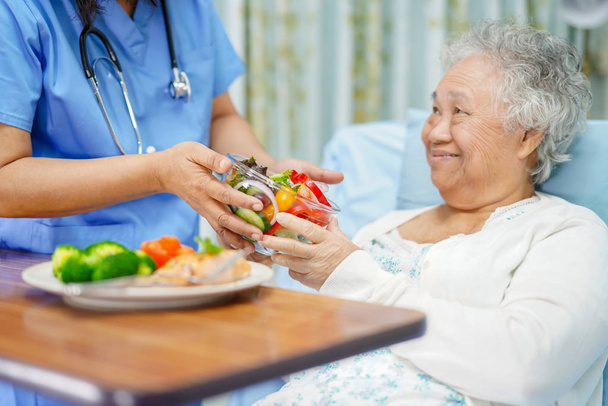 Asiatico anziano o anziano donna anziana paziente mangiare la colazione cibo sano con speranza e felice mentre seduto e affamato sul letto in ospedale
 - Foto, immagini