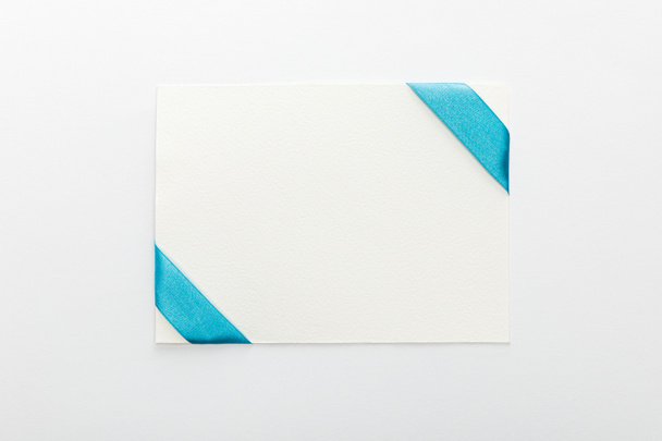 top view of blank card with blue decorative satin ribbon on white background - Fotografie, Obrázek