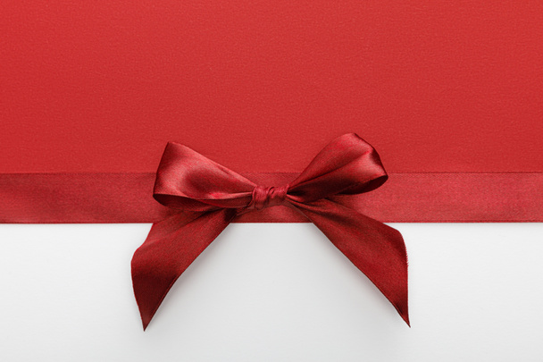 top view of satin burgundy decorative ribbon with bow on white and red background - Photo, Image