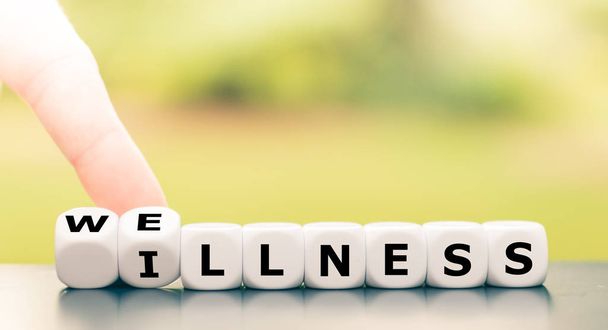 Hand turns dice and changes the word "illness" to "wellness". - Foto, afbeelding