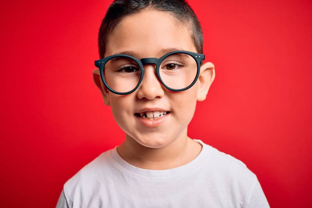 Nuori pieni fiksu poika lapsi yllään nörtti lasit yli punainen eristetty tausta onnellinen kasvot seisoo ja hymyilee luottavainen hymy osoittaa hampaat
 - Valokuva, kuva