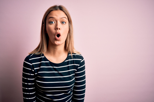 Young beautiful blonde woman wearing casual striped sweater over pink isolated background afraid and shocked with surprise expression, fear and excited face. - 写真・画像