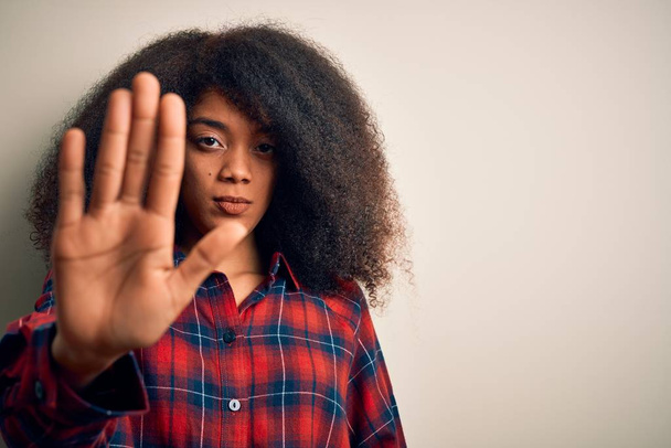 Jonge mooie Afrikaanse Amerikaanse vrouw draagt casual shirt over geïsoleerde achtergrond doen stoppen met zingen met palm van de hand. Waarschuwingsuitdrukking met negatief en ernstig gebaar op het gezicht. - Foto, afbeelding