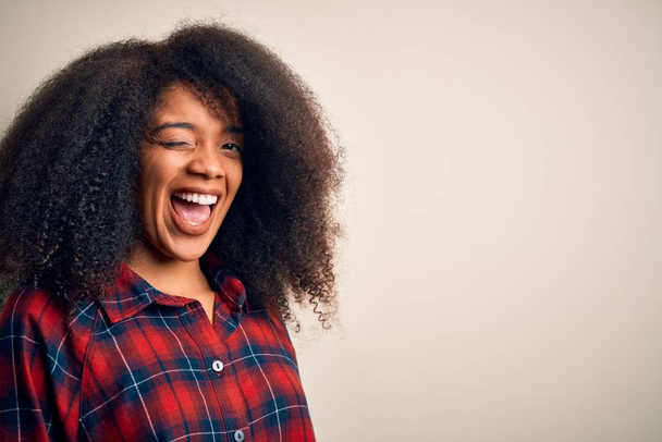 Young beautiful african american woman wearing casual shirt over isolated background winking looking at the camera with sexy expression, cheerful and happy face. - Foto, immagini