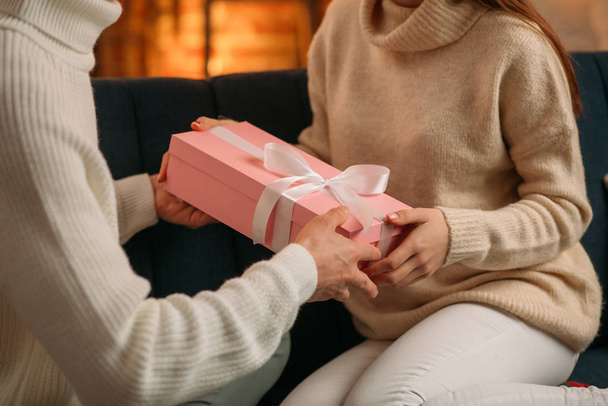 Handsome man presenting a gift to his beautiful girlfriend and smiling. Beautiful young couple at home enjoying spending time together.Valentines Day, relationships and people concept - Foto, Bild