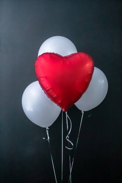 Red heart-shaped balloon and white round air balloons on a black background. Valentines Day, holiday, love. Place for text, vertical photo. - Photo, Image