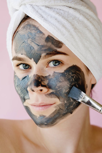 Young woman apply clay facial mask. Face peeling mask with charcoal, spa beauty treatment, skincare, cosmetology. Close up - Photo, Image