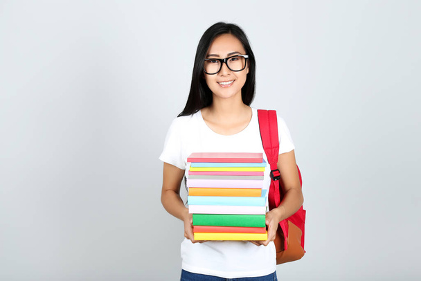 Young woman with stack of books and backpack on grey background - Foto, Imagem