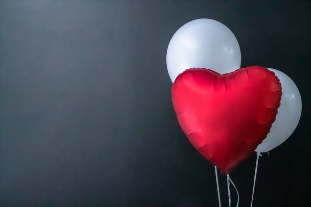 Red heart-shaped balloon and white round air balloons on a black background. Valentines Day, holiday, love. - Fotografie, Obrázek