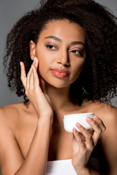 tender african american girl applying face cream, isolated on grey - Photo, Image