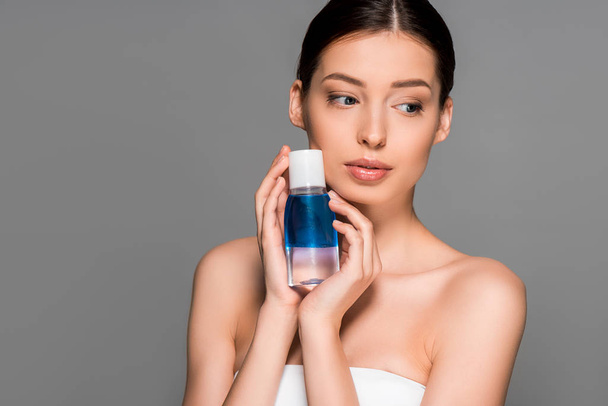 portrait of beautiful girl holding bottle of makeup remover, isolated on grey - Fotoğraf, Görsel