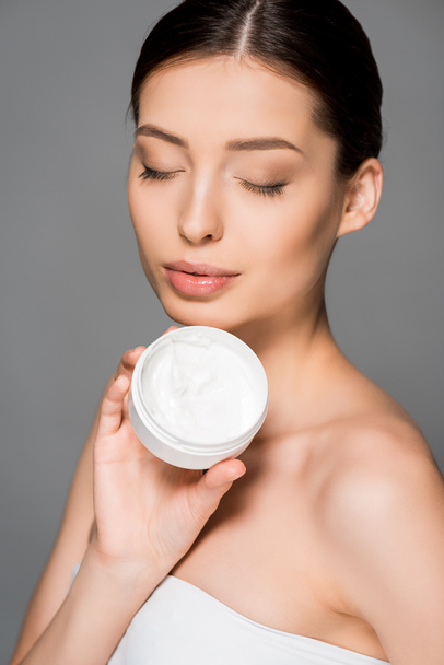 beautiful girl with closed eyes holding moisturizing cream, isolated on grey - Photo, Image