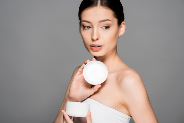 attractive girl holding plastic container with face cream, isolated on grey - Фото, зображення