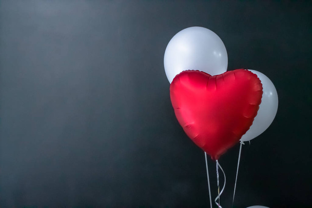 Red heart-shaped balloon and white round air balloons on a black background. Valentines Day, holiday, love. - Foto, Bild