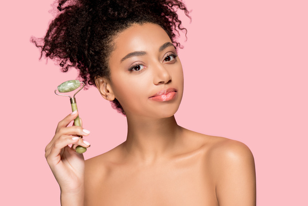 beautiful naked african american girl using jade roller, isolated on pink - Photo, Image