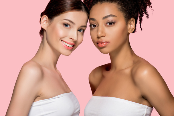 Porträt lächelnder multikultureller Mädchen mit sauberer Haut, isoliert auf rosa - Foto, Bild