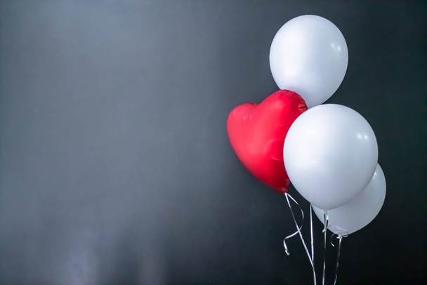 Red heart-shaped balloon and white round air balloons on a black background. Valentines Day, holiday, love. - Φωτογραφία, εικόνα