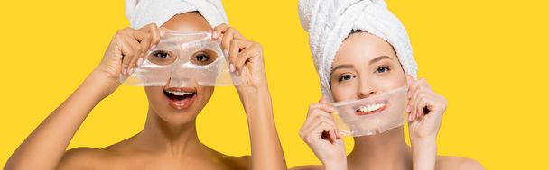 panoramic shot of cheerful multicultural girls holding hydrogel masks, isolated on yellow - Foto, Bild
