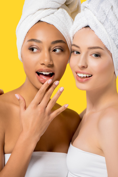 surprised multicultural girls with towels on heads, isolated on yellow - Foto, Imagen