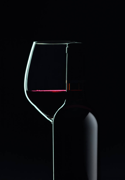 Κλειστό μπουκάλι και ποτήρι κόκκινο κρασί σε μαύρο φόντο.  - Φωτογραφία, εικόνα